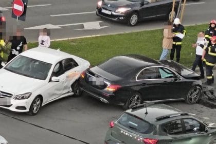 White car and black sedan collide at an intersection; firefighters and bystanders assess the scene.