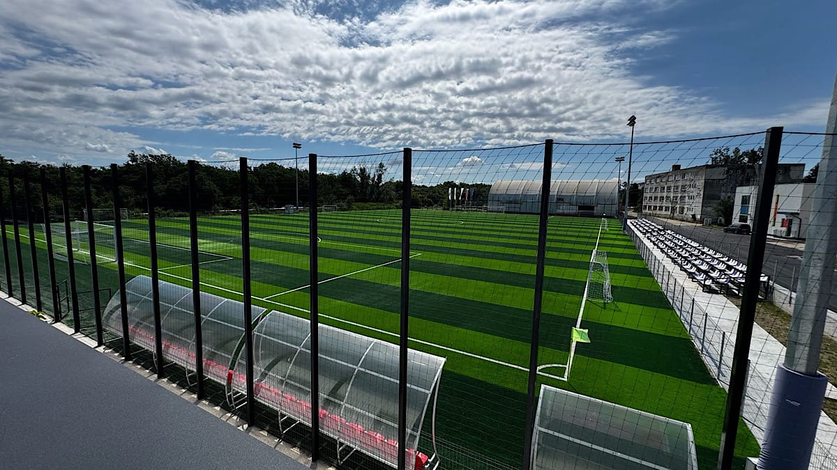 Baza Sportiva Pitesti Anghel Saligny Stiripitesti.ro Wide view of an outdoor soccer field with artificial turf, fenced perimeter, and empty stands along the right under a cloudy sky baza sportiva pitesti anghel saligny